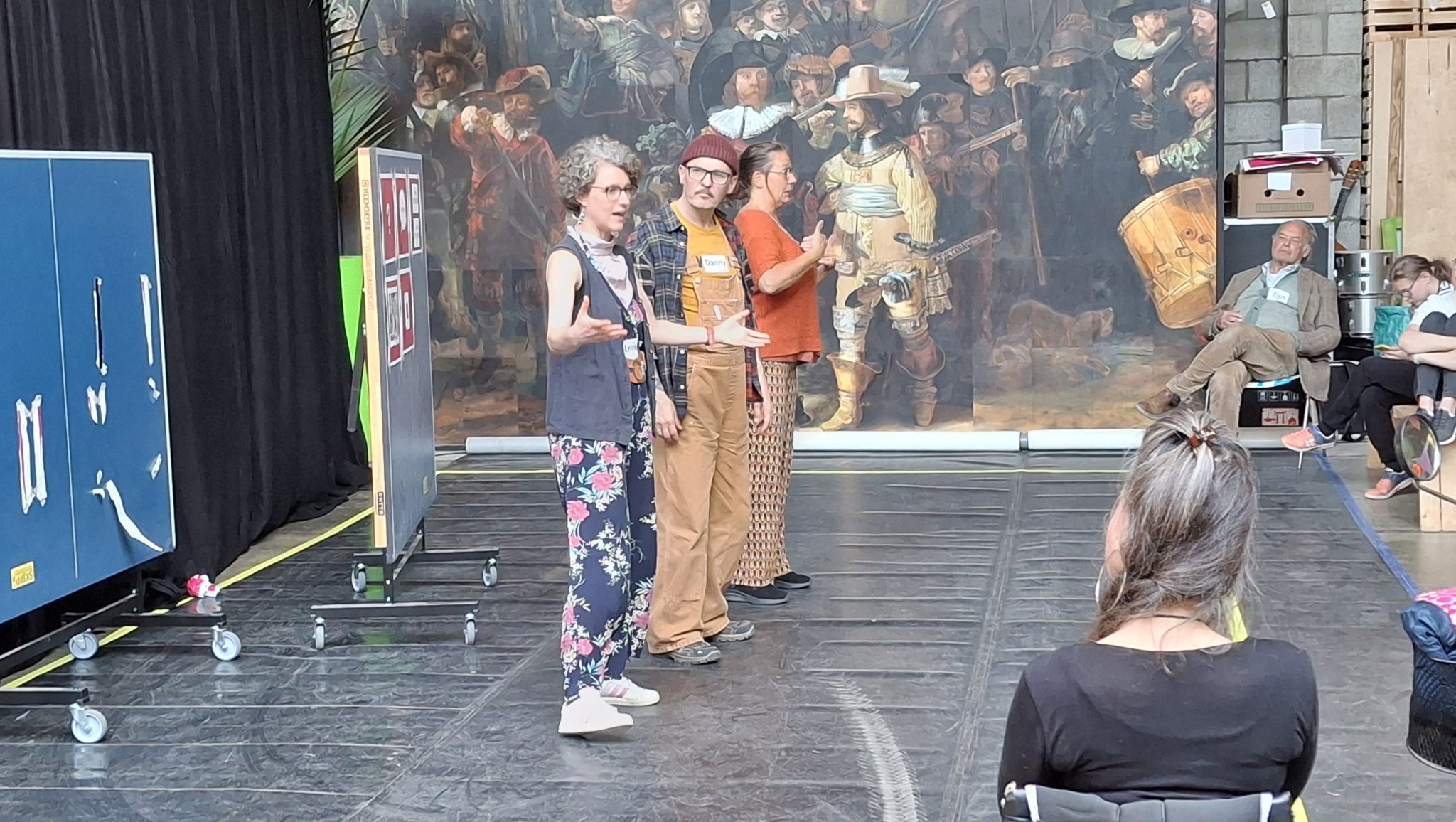 Drie mensen op theaterpodium tijdens voorstelling.